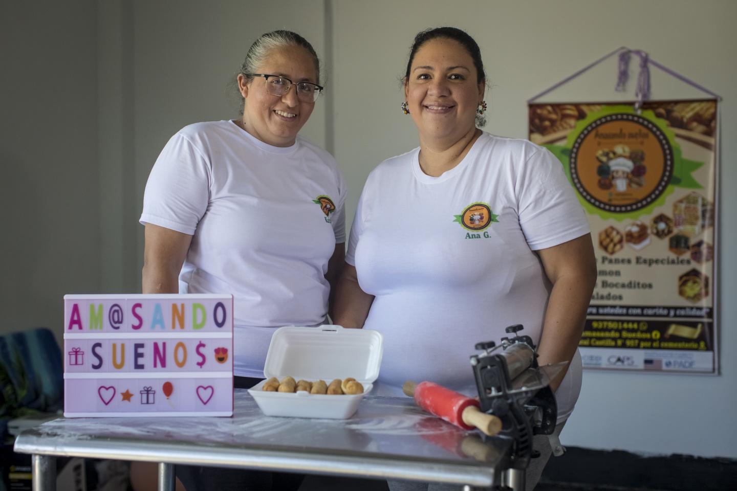 Kathy y Ana posan frente a la cámara con un plato de tequeños y un cartel con el nombre de su negocio: "Amasando Sueños"