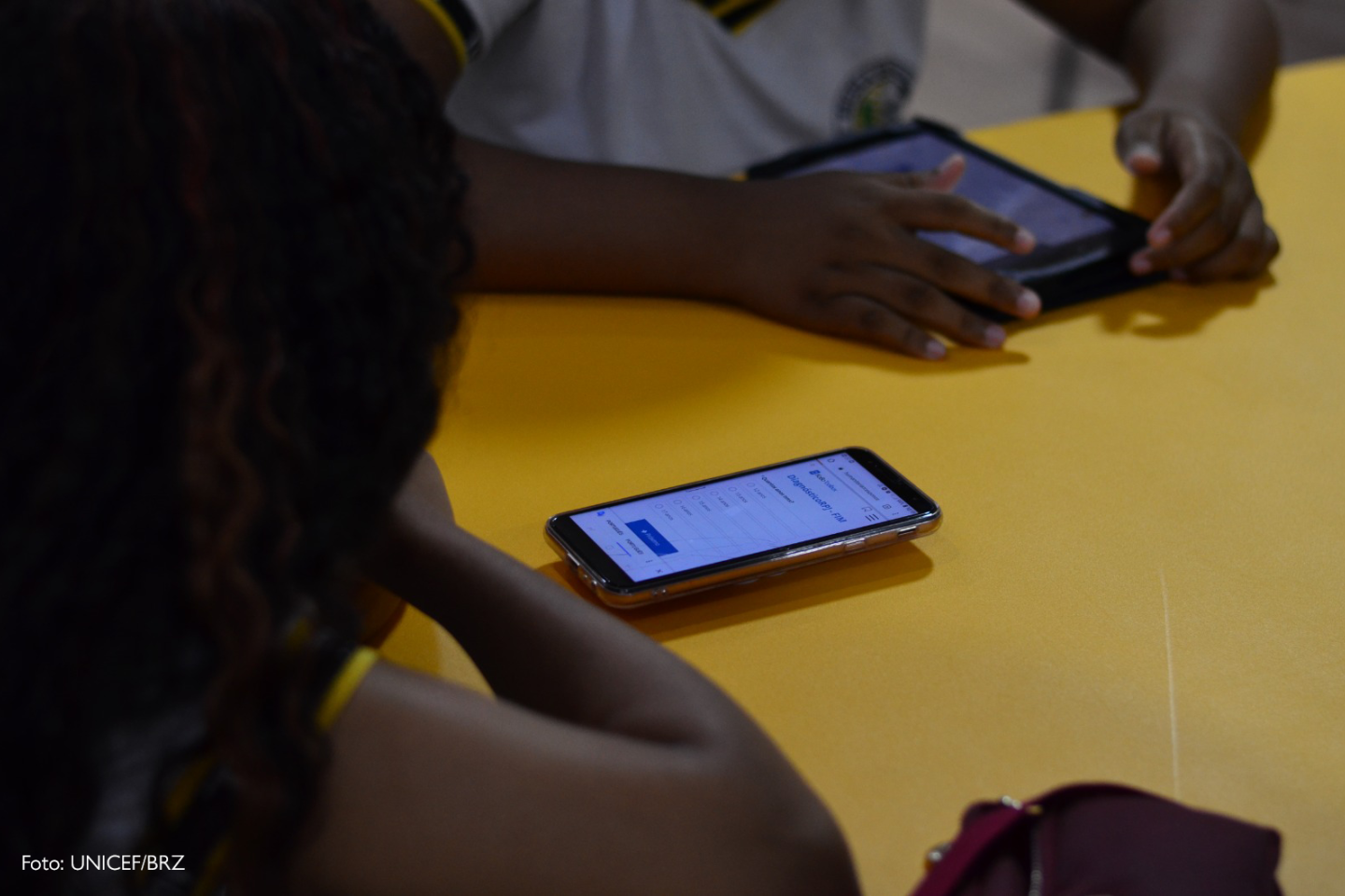 Duas pessoas jovens respondendo a pesquisa no celular e o crédito da imagem (UNICEF/BRZ) anotado no canto esquero